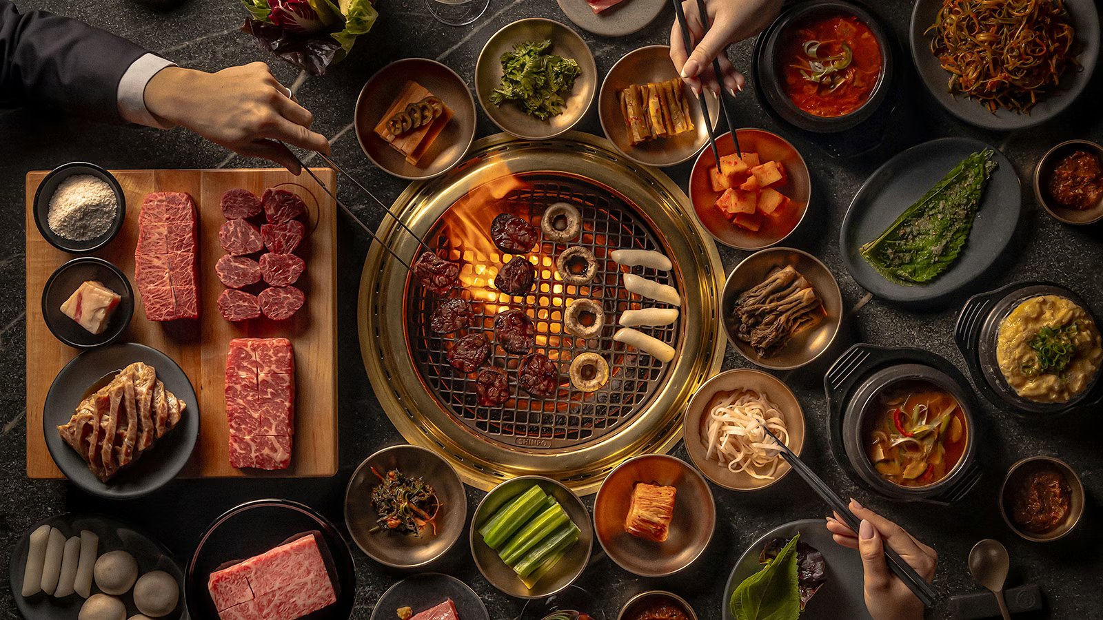 한국식 바비큐 불판과 프라임 고기, 반찬이 한 상 가득 차려진 모습