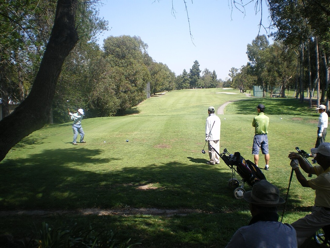 Golfers teeing off on a tree-lined fairway at Rancho Park Golf Course
